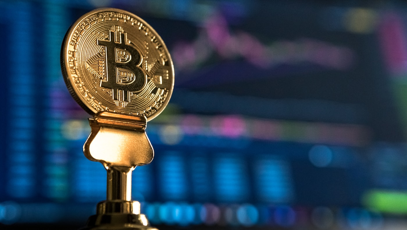 A Bitcoin coin on a stand against a market chart